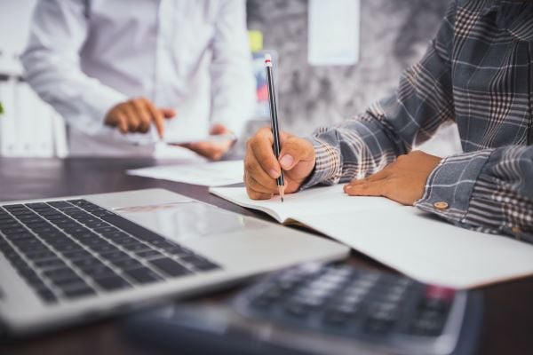 people making notes on laptop - knowing what data you have is crucial when building a data dictionary