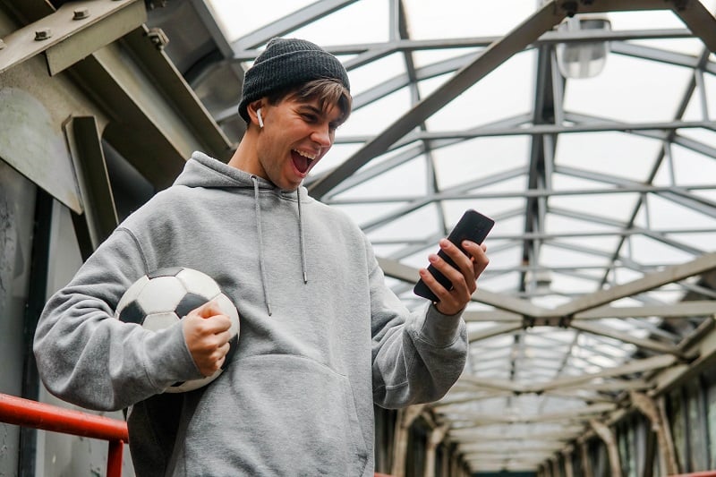 Man on phone with football celebrating - sports betting websites may need more up-to-the-minute data
